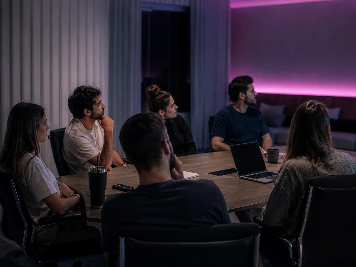 Six people in a meeting room following a training session, the back wall washed in magenta light